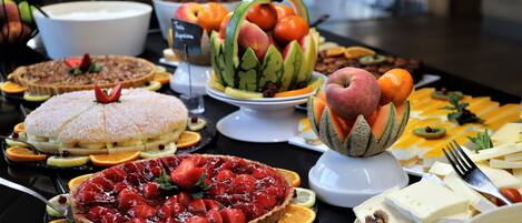 Un bufé con diversos alimentos, entre ellos tartas, frutas y quesos.