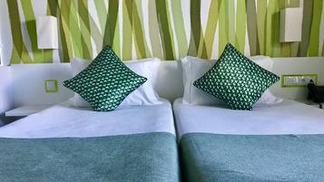 A hotel room with two beds, each with a green patterned pillow and a white headboard.