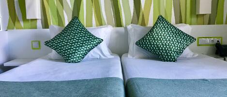 A hotel room with two beds, each with a green patterned pillow and a white headboard.