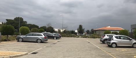 A parking lot with several cars, paved ground, and a building with a red roof in the background.