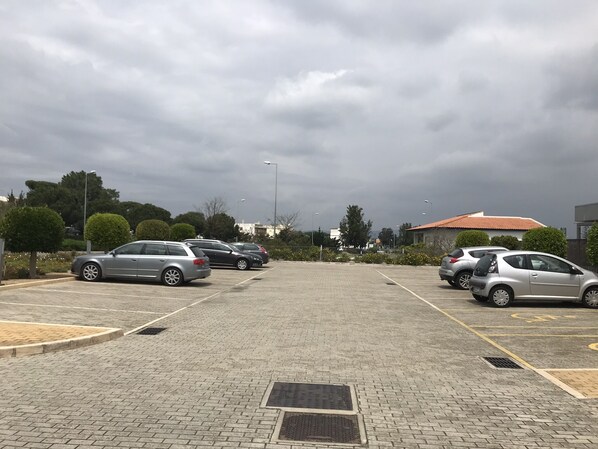 A parking lot with several cars, paved ground, and a building with a red roof in the background. - Hotel 3K Faro Aeroporto (Faro)