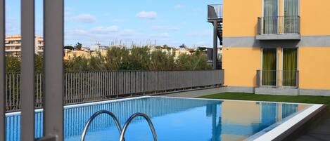 A swimming pool with metal ladders, surrounded by a wooden deck and a fence.