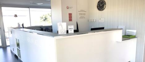 A reception desk with a clock, informational signs, and a window with a view of trees.