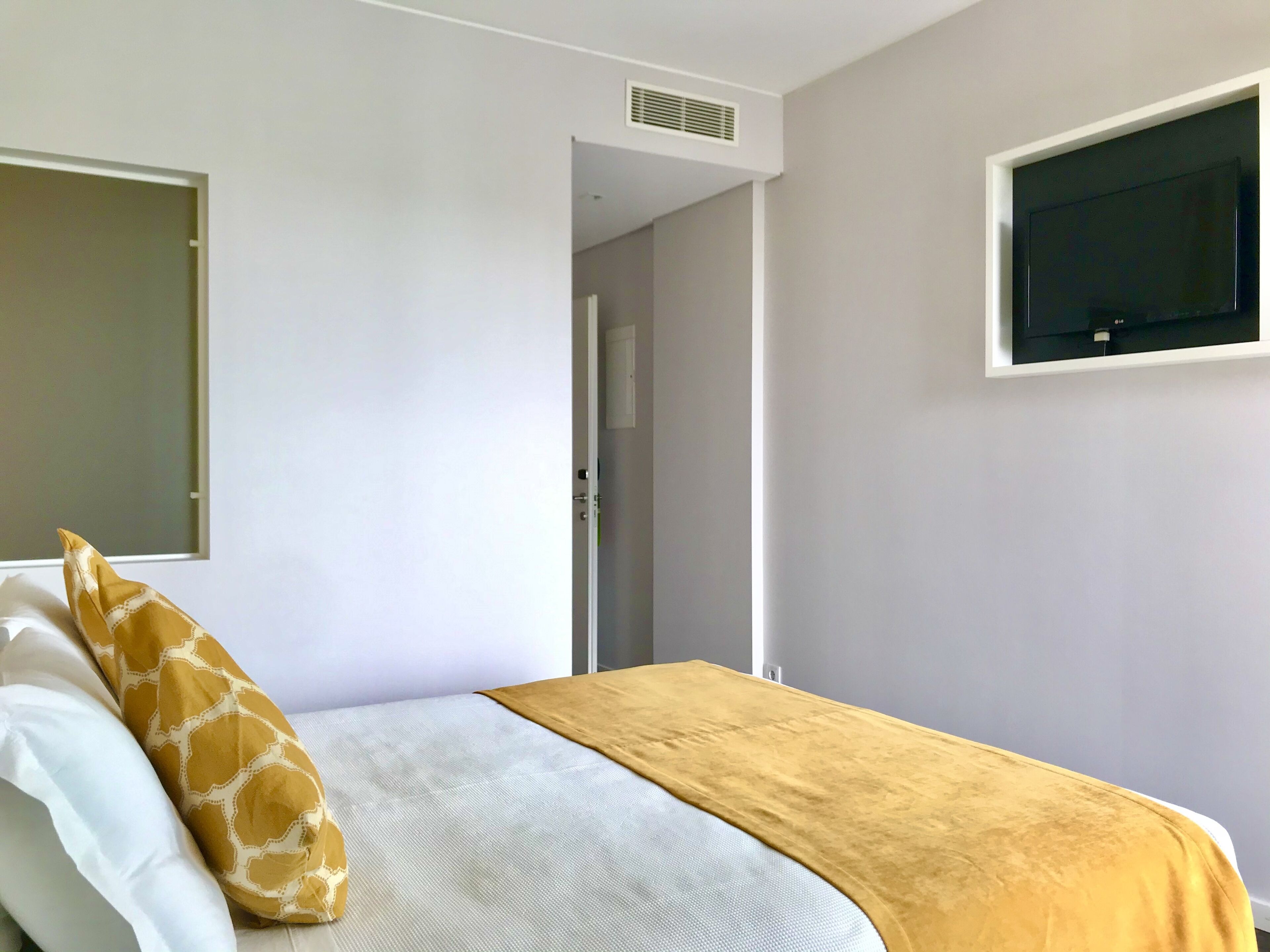 Ein Schlafzimmer mit einem Bett, einem an der Wand montierten Fernseher und einer Tür zu einem weiteren Raum.