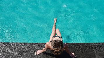 Una persona recostada sobre una superficie negra junto a una piscina turquesa.