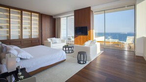 A modern hotel room with a large bed, a seating area with a TV, and a balcony with a view. - Olympic Residence (Limassol)