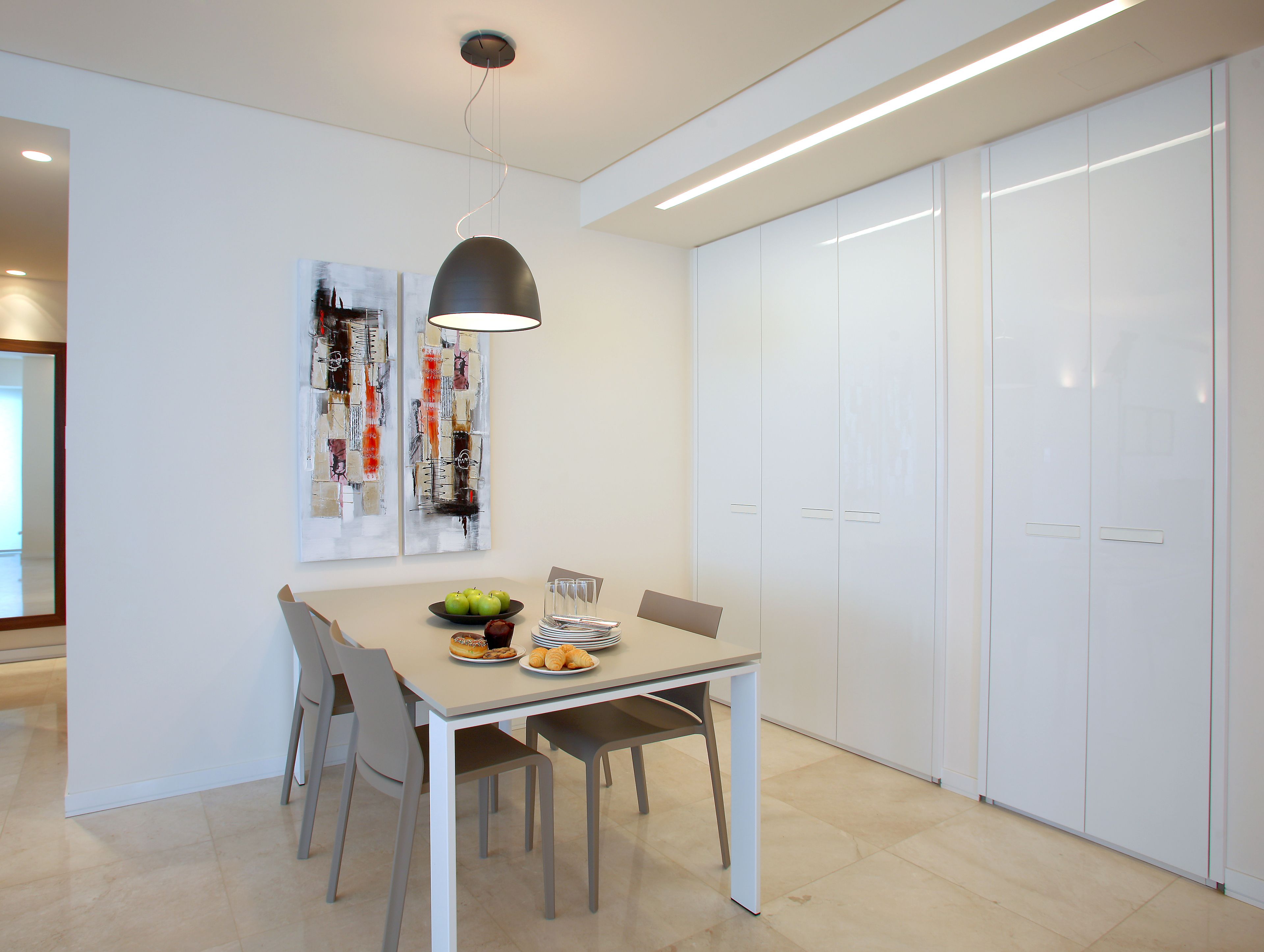 Un comedor moderno con una mesa dispuesta para cuatro, una lámpara colgante y un armario blanco al fondo.