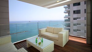 A balcony with a view of the sea, a white cushioned sofa, and a glass coffee table with bottles. - Olympic Residence (Limassol)