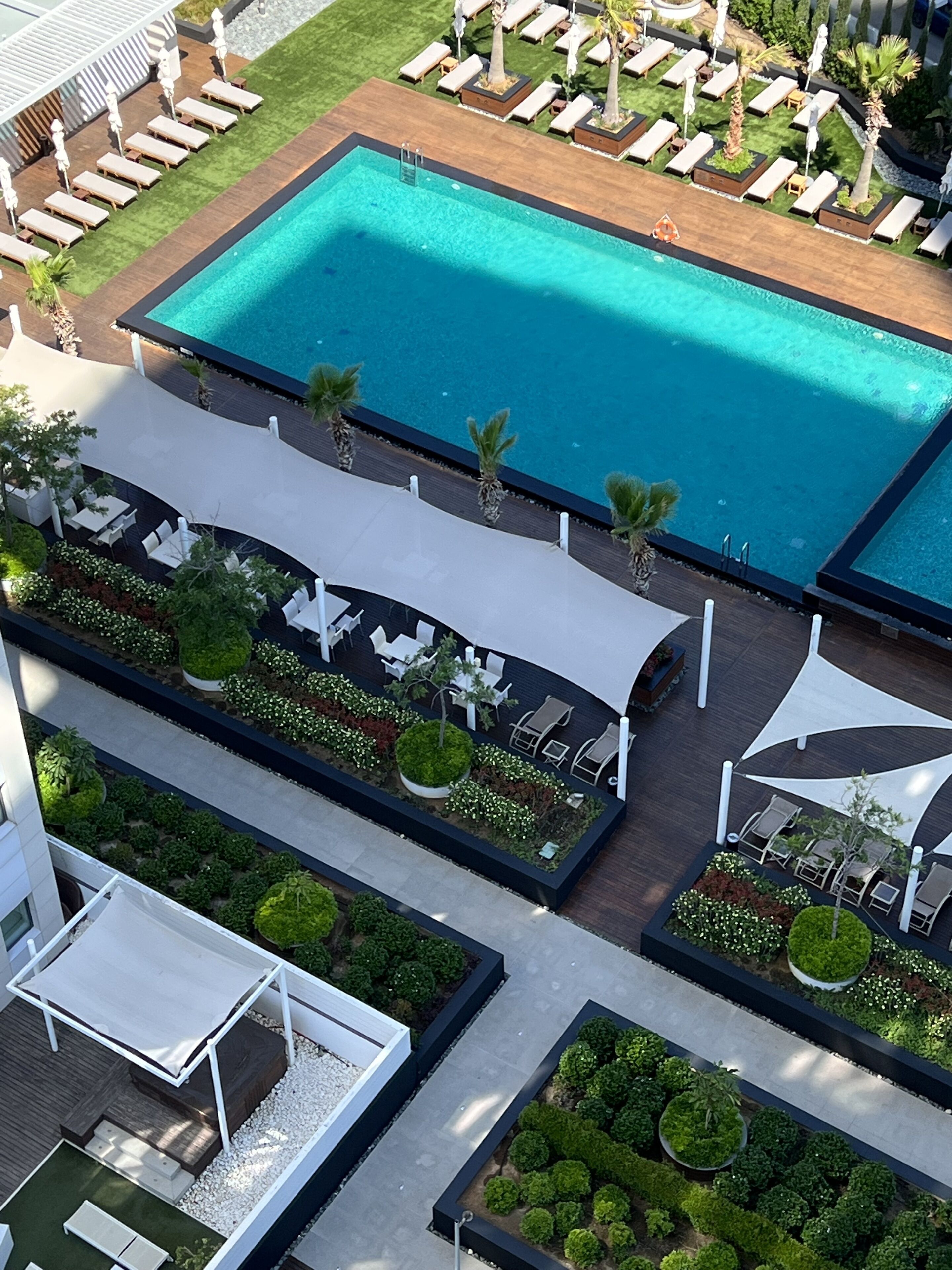 An aerial view of a resort with a large swimming pool, sun loungers, and a landscaped garden area.