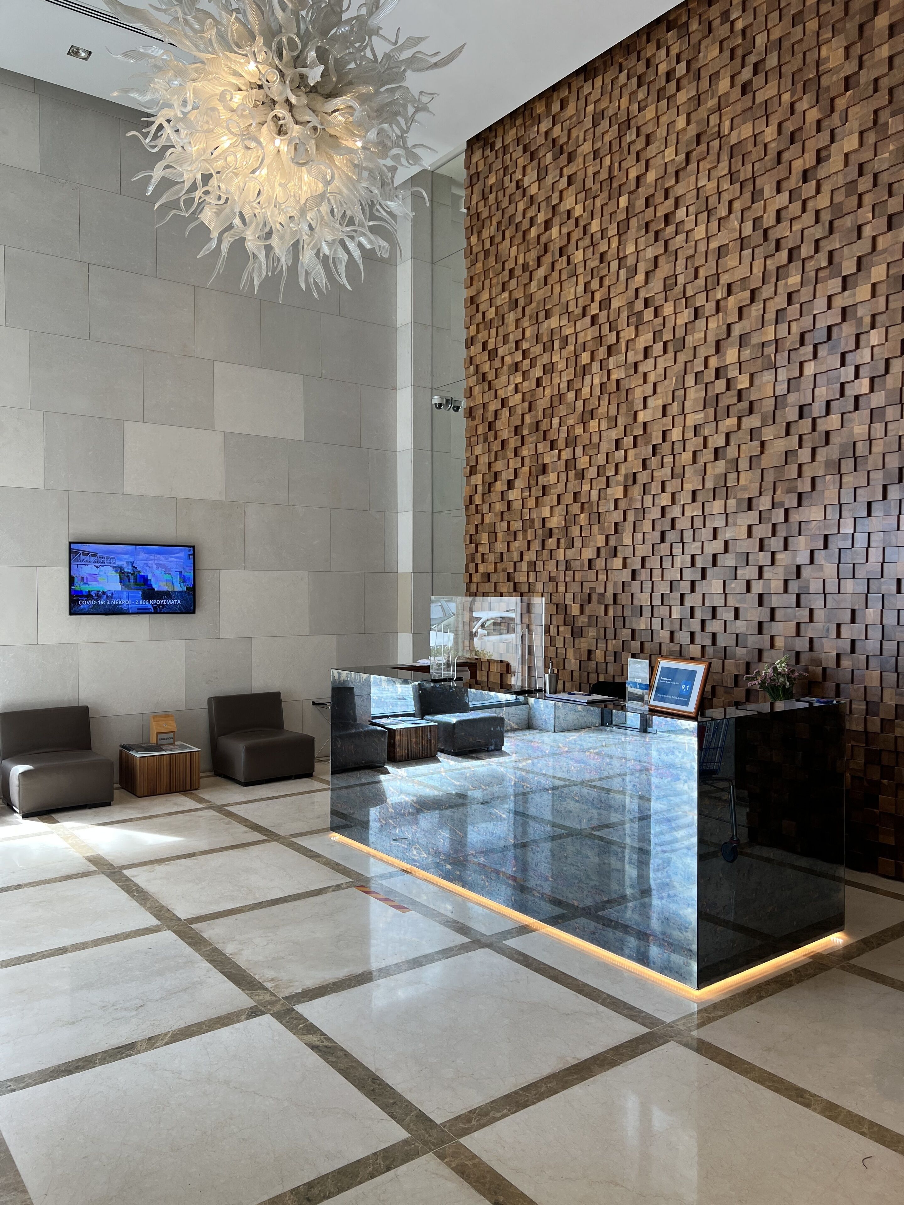 Un lobby moderno con mostrador de recepción, zona de estar y una gran lámpara decorativa.
