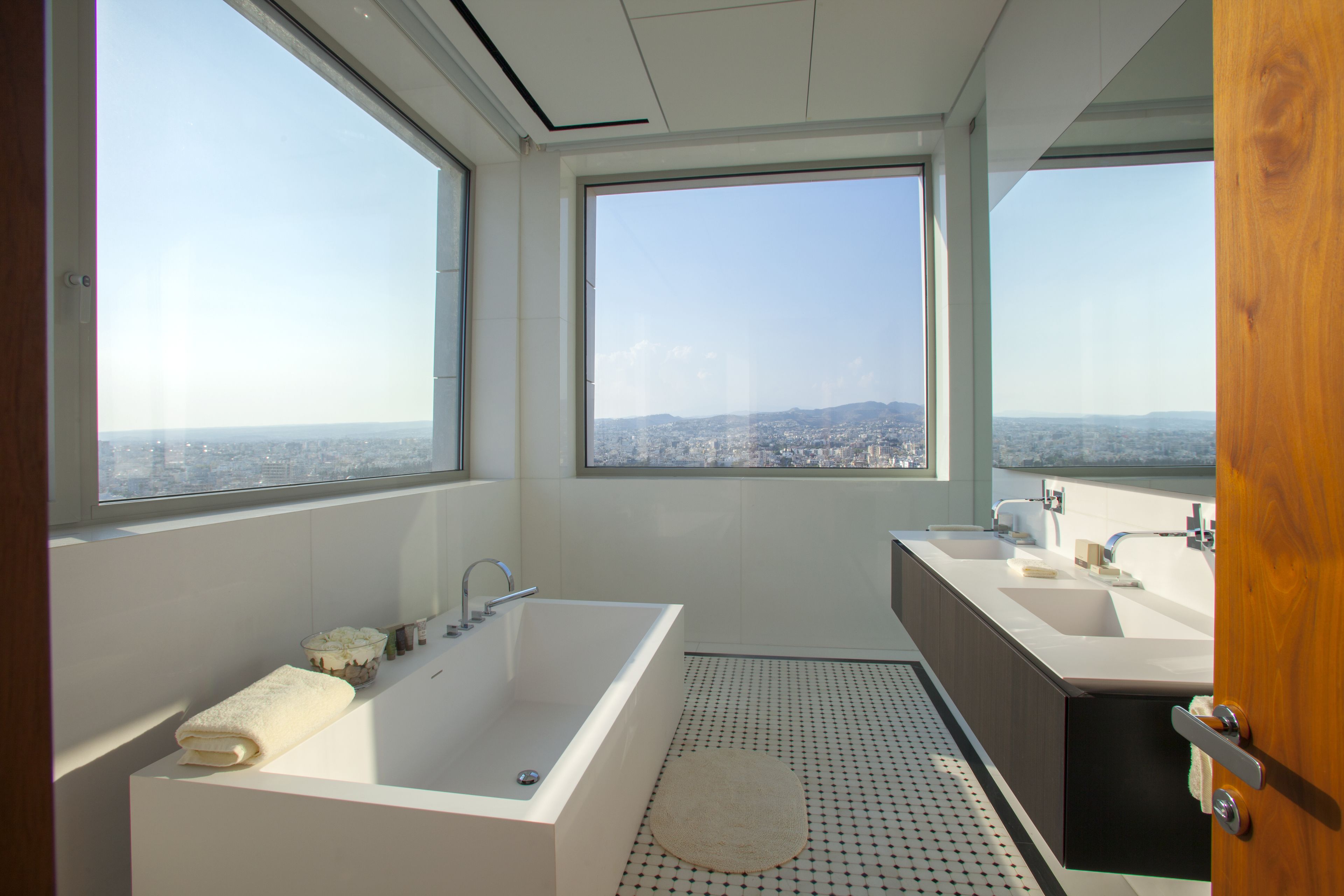 Un bagno moderno con una vasca da bagno ampia, due lavandini e vista sulla città attraverso grandi finestre.