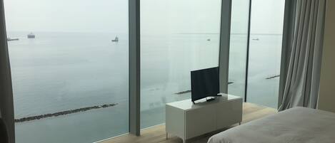 A modern hotel room with a large window offering a view of the sea and ships.