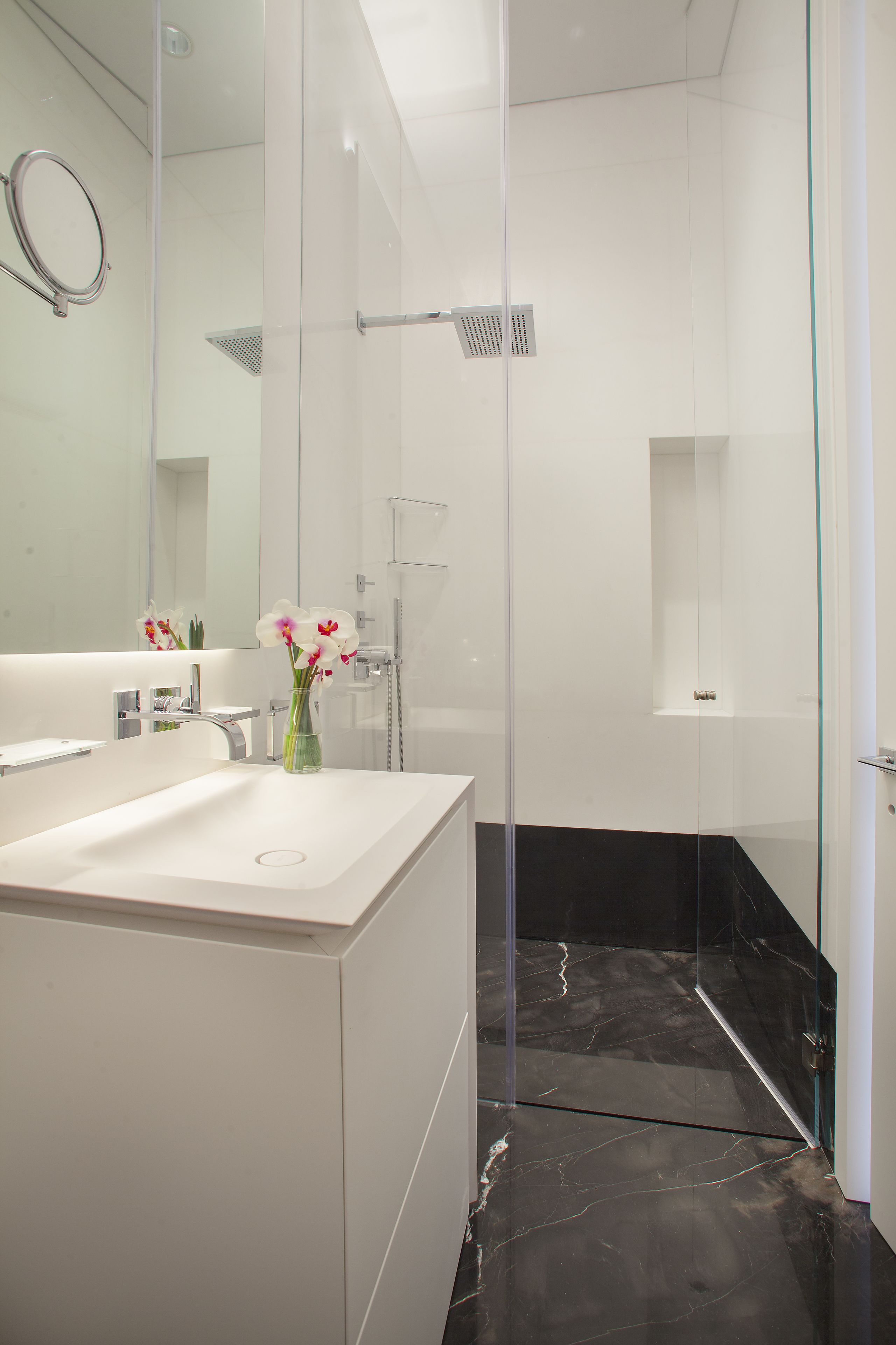 A modern bathroom with a glass-enclosed shower, a white sink, and a vase with flowers.