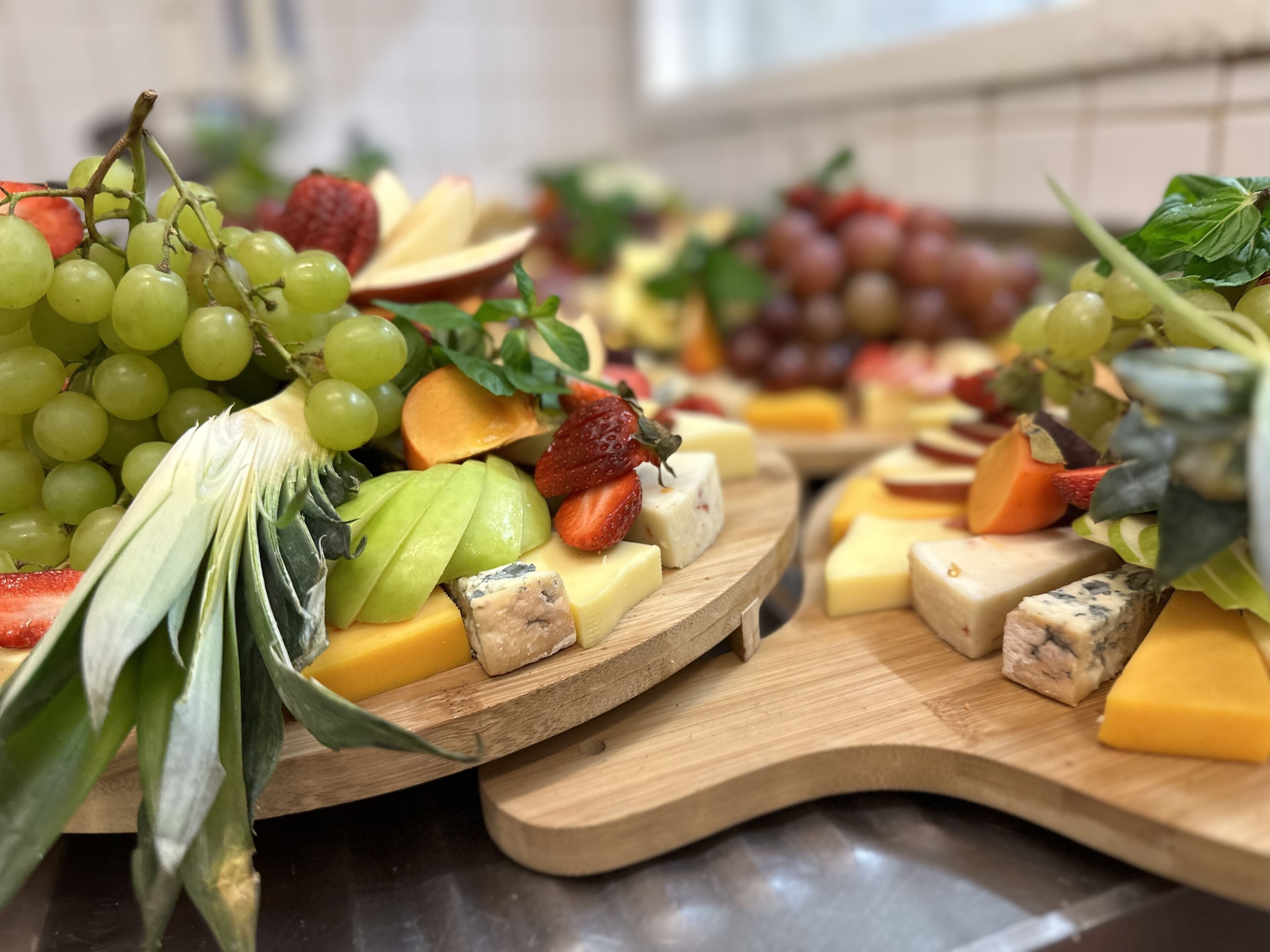 A wooden board with various cheeses, fruits, and grapes.