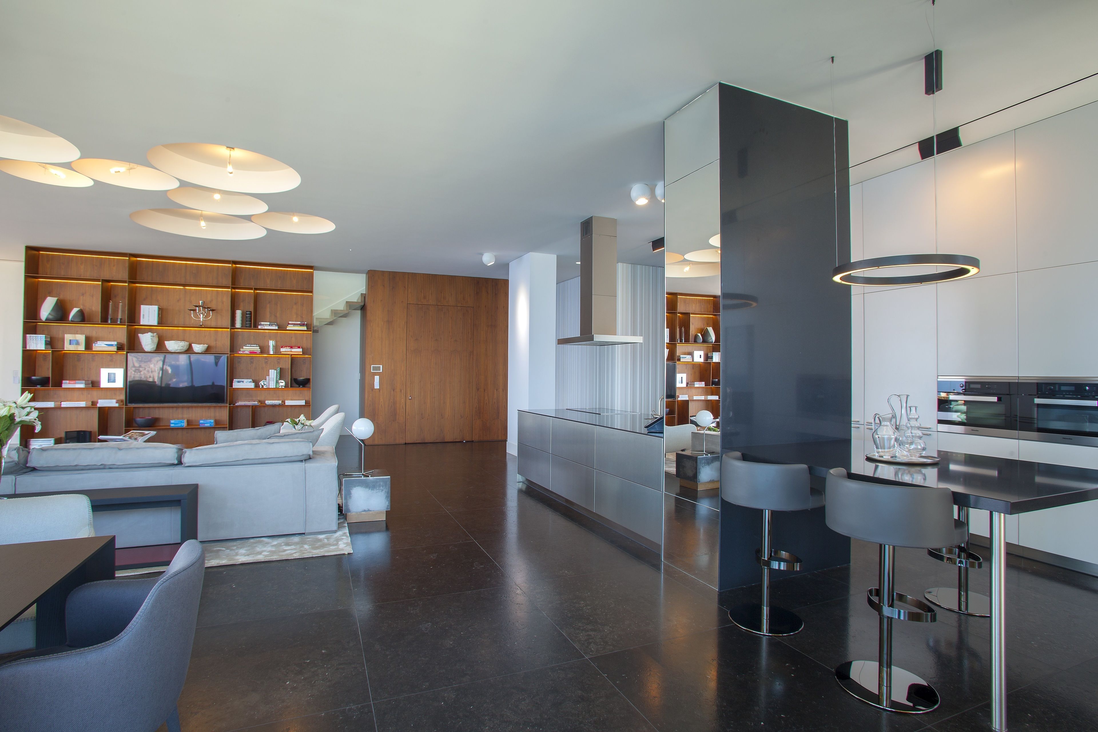 A modern kitchen with a built-in oven, a dining area with a bar, and a living room with a large TV and seating.