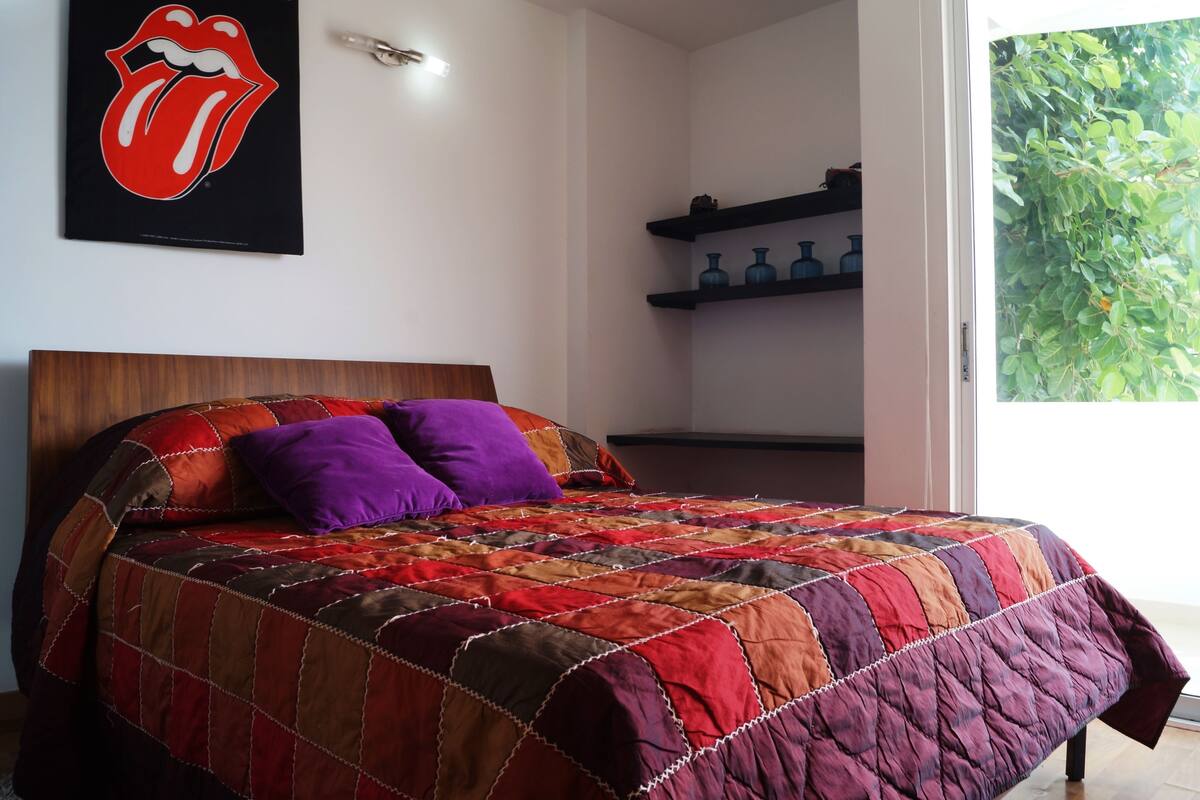 A bedroom with a large bed, a headboard, and a window with a view of greenery.