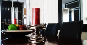 Una mesa de comedor con un cuenco de fruta, una vela roja y un candelabro metálico.