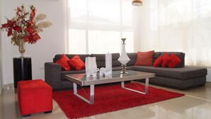 A modern living room with a grey sofa, red cushions, a glass coffee table, and a red rug. - Casa Blanca del Mar Hotel Boutique (Cartagena)