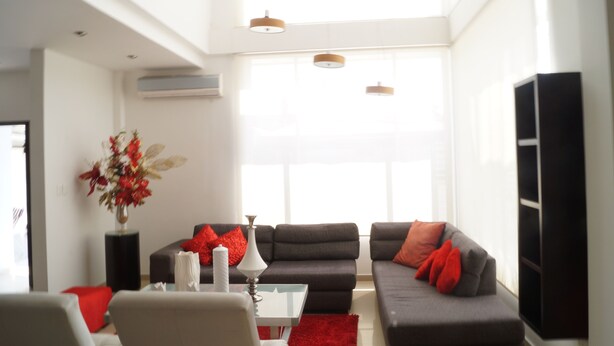 A modern living room with a grey sofa set, red cushions, a white vase with flowers, and a glass coffee table. - Casa Blanca del Mar Hotel Boutique (Cartagena)