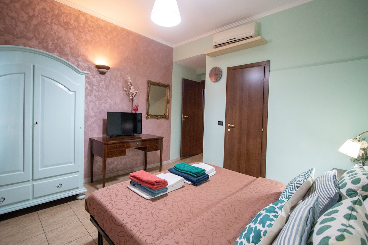 A bedroom with a bed, a wardrobe, a desk, a television, and a mirror.