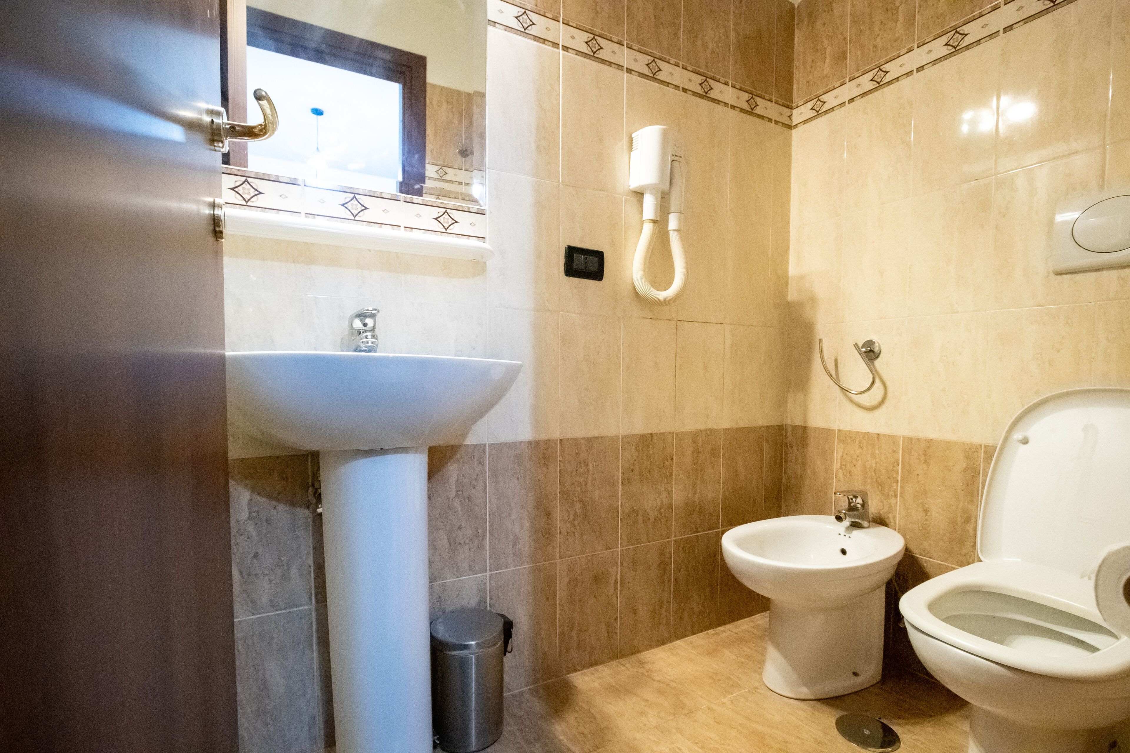 A bathroom with a sink, bidet, toilet, and a trash bin.