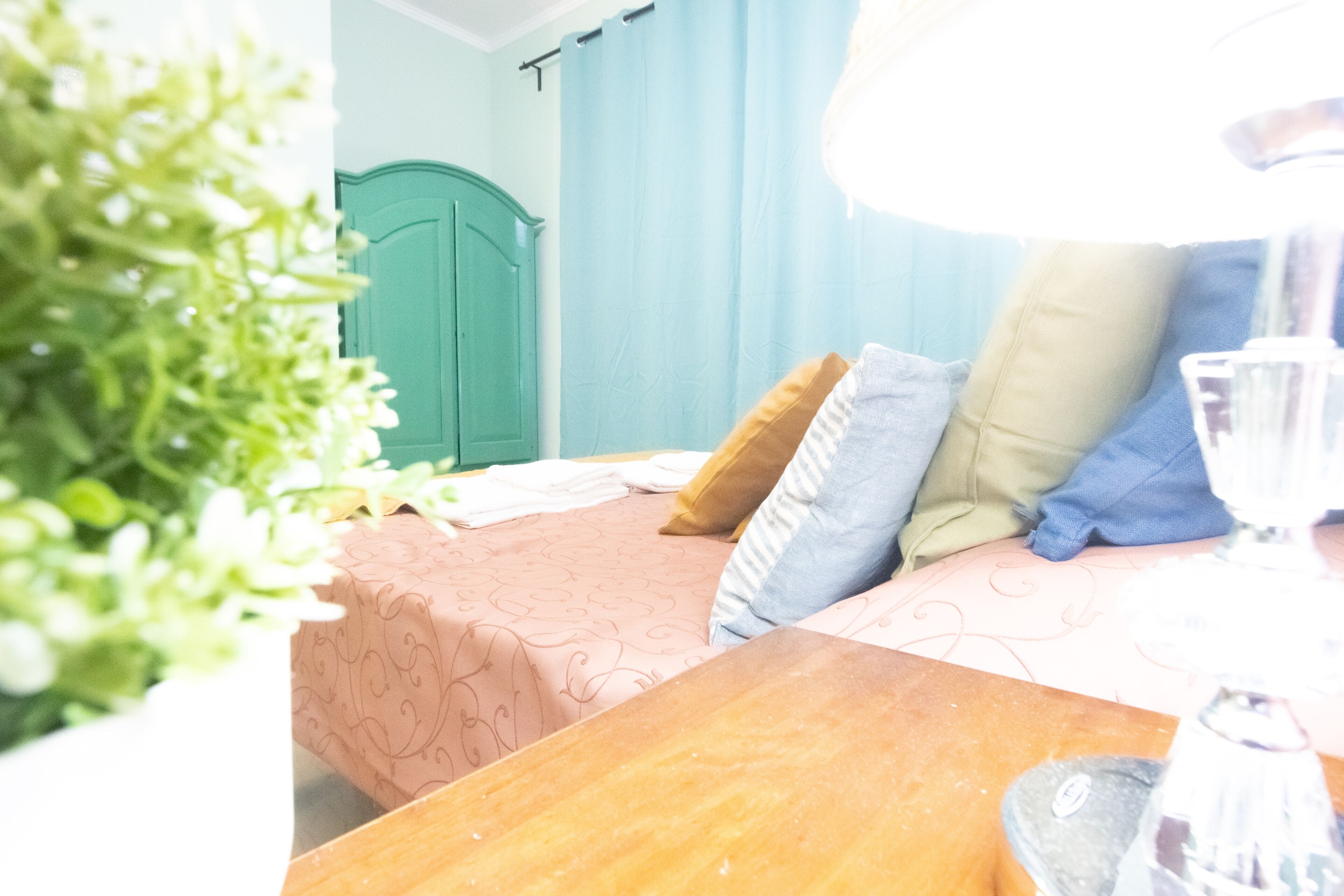 Un dormitorio con cama, una mesita de noche de madera, un armario verde y una ventana con cortinas.