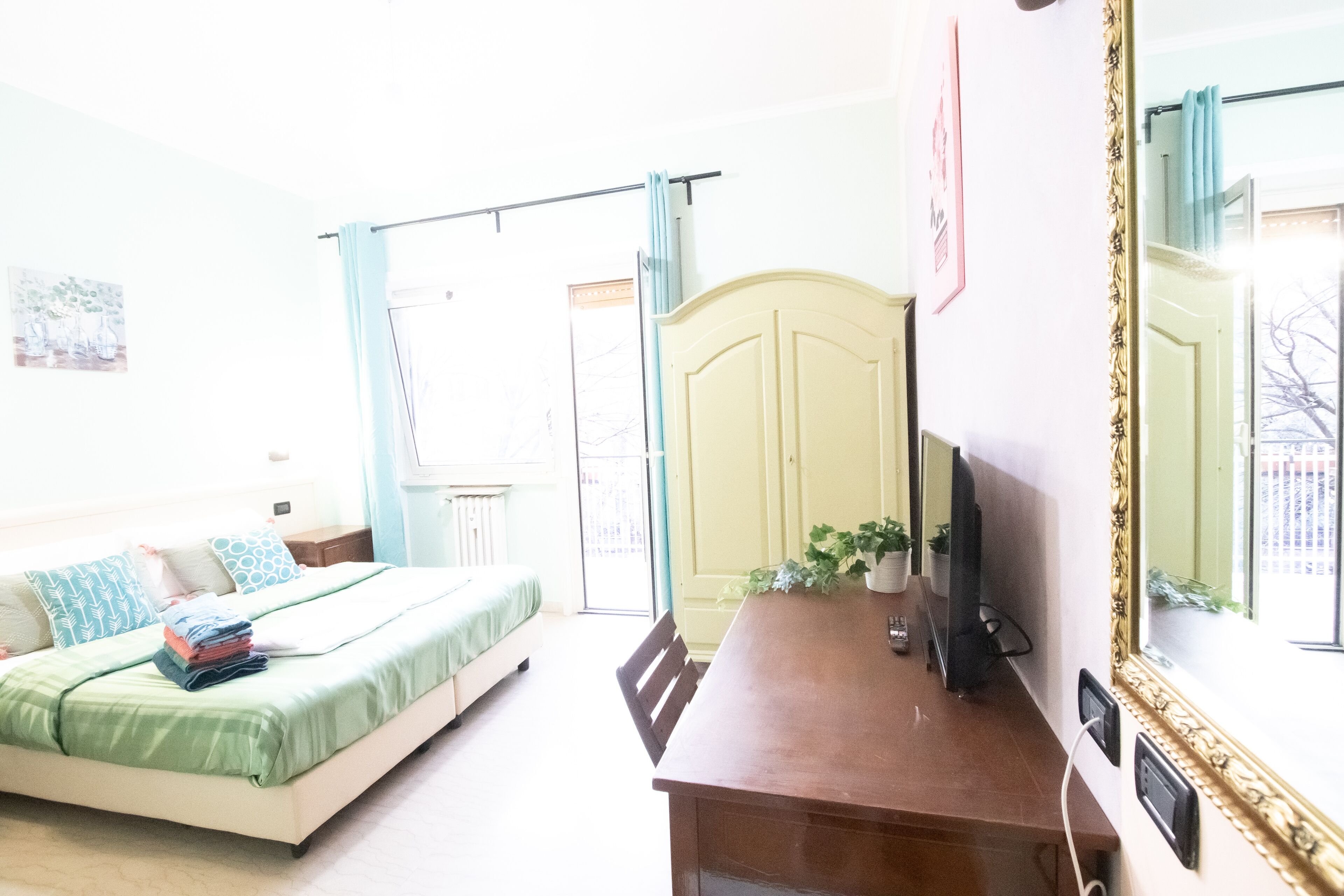 A bedroom with a bed, a desk, a television, and a mirror.