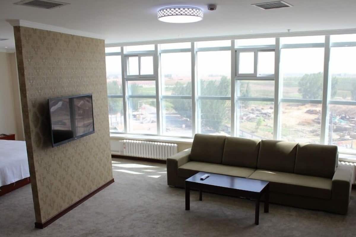 A room with a sofa, a small table, a TV mounted on the wall, and large windows with a view of the outside.