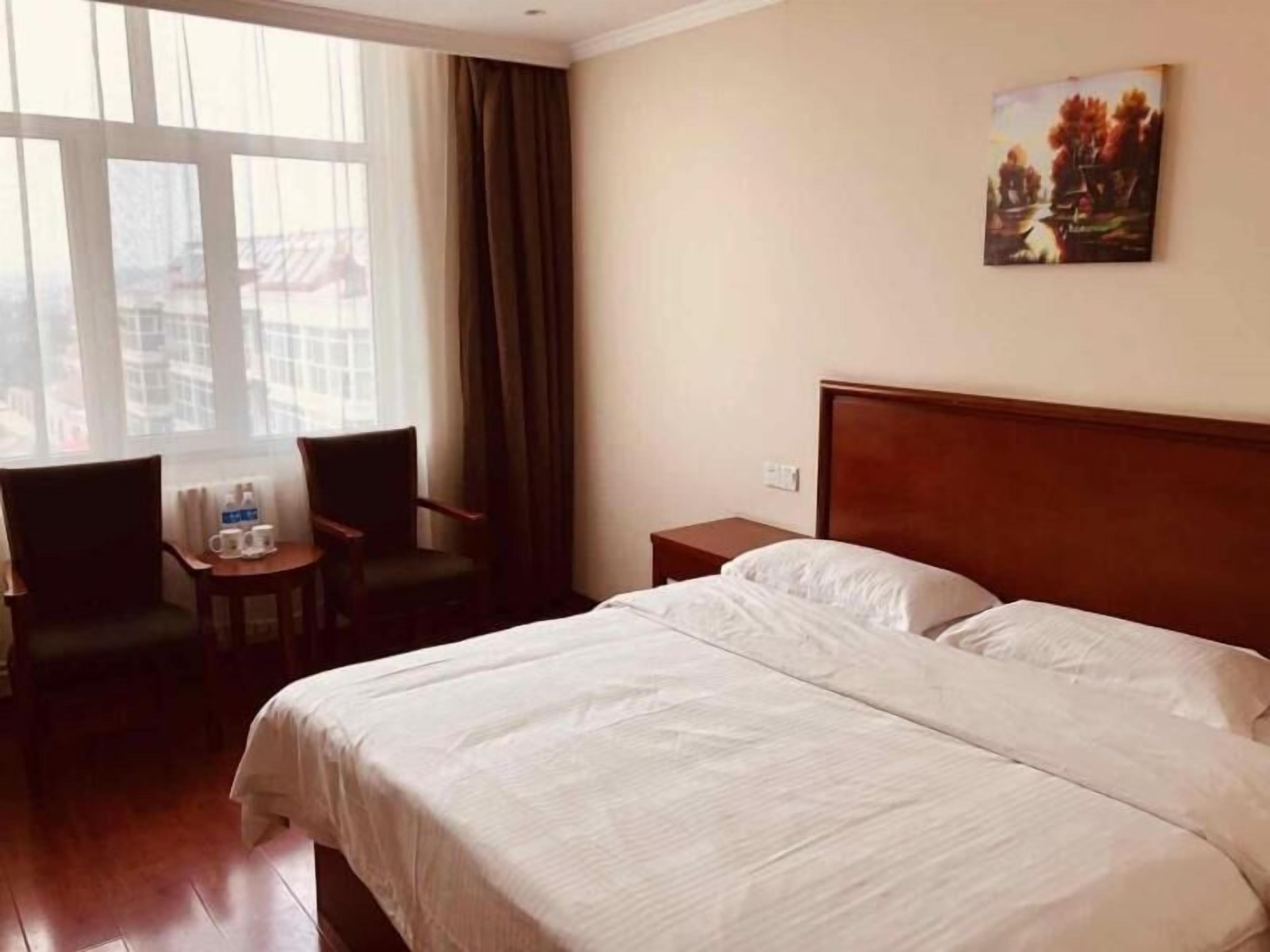 A hotel room with a large bed, a small table with two chairs, a window with curtains, and a painting on the wall.
