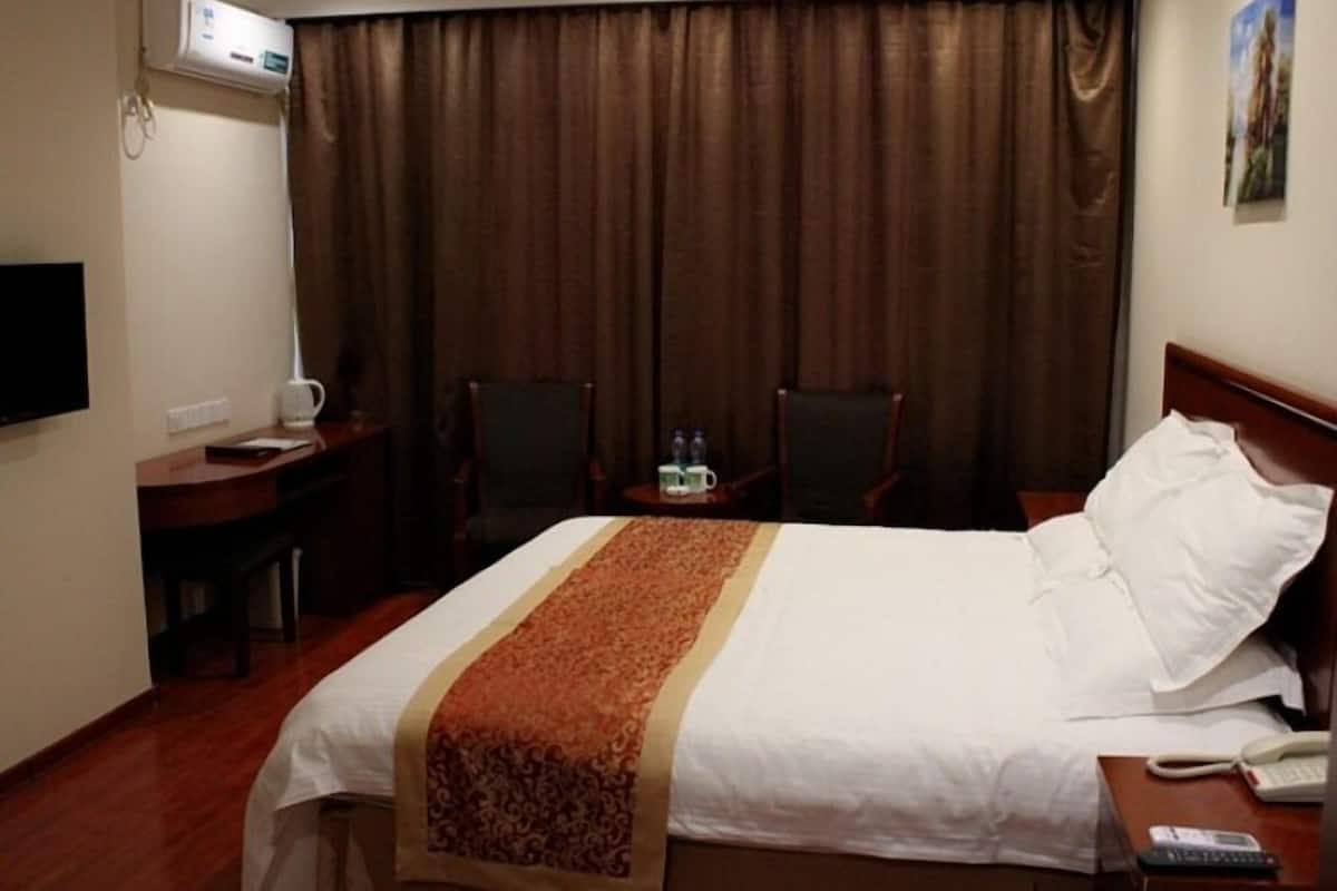 A hotel room with a bed, a desk, two chairs, a TV, and an air conditioning unit.
