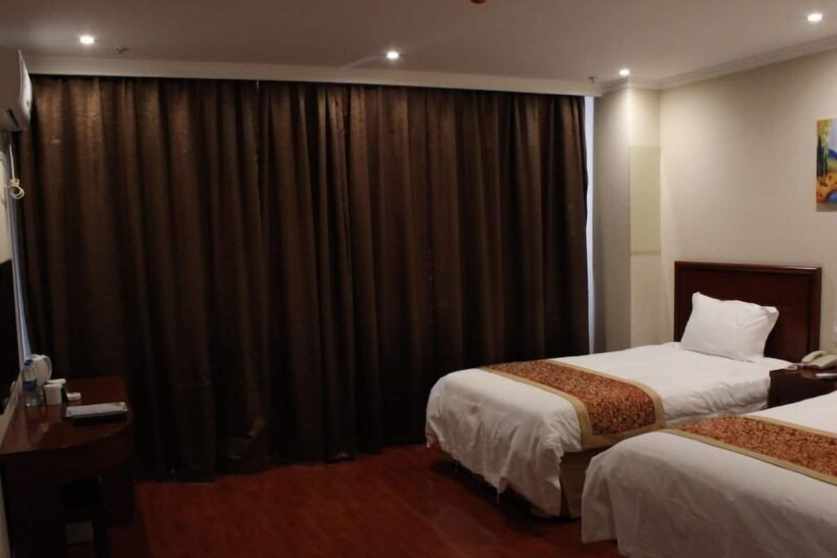 A hotel room with two beds, a desk, and a large window with curtains.