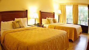 A hotel room with two beds, each with a wooden headboard, a nightstand with a lamp, and a window with curtains.
