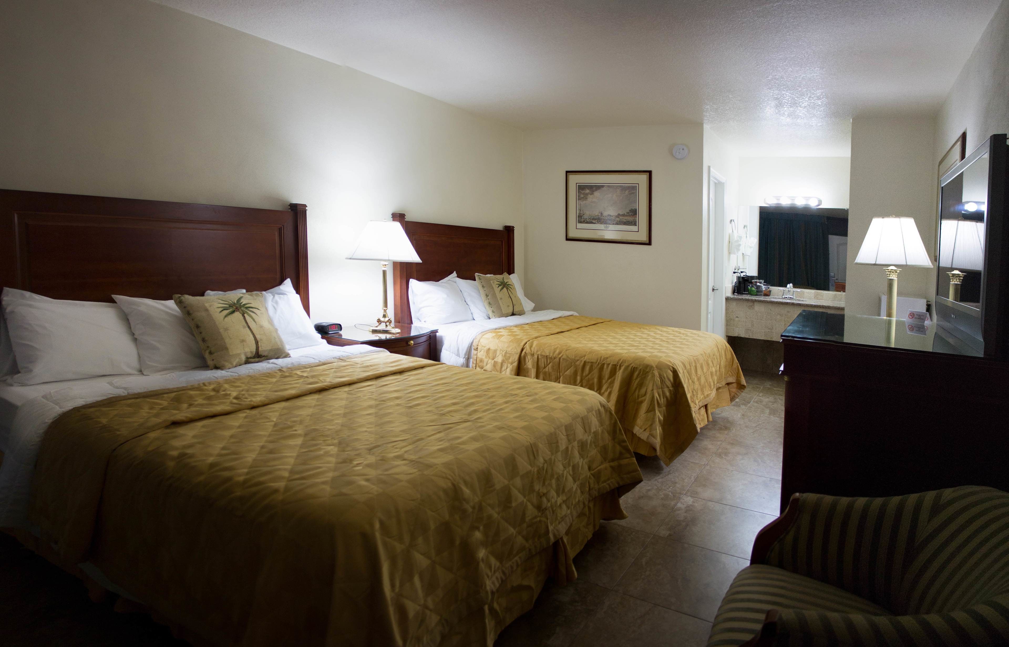 A hotel room with two beds, a desk, a chair, a mirror, and a bathroom visible through an open door.