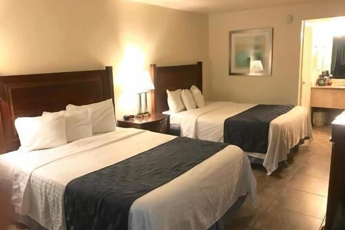 Habitación de hotel con dos camas, una mesita de noche, una lámpara y un cuadro en la pared.
