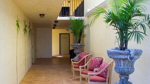 A corridor with stone flooring, wicker chairs with red cushions, and potted plants.