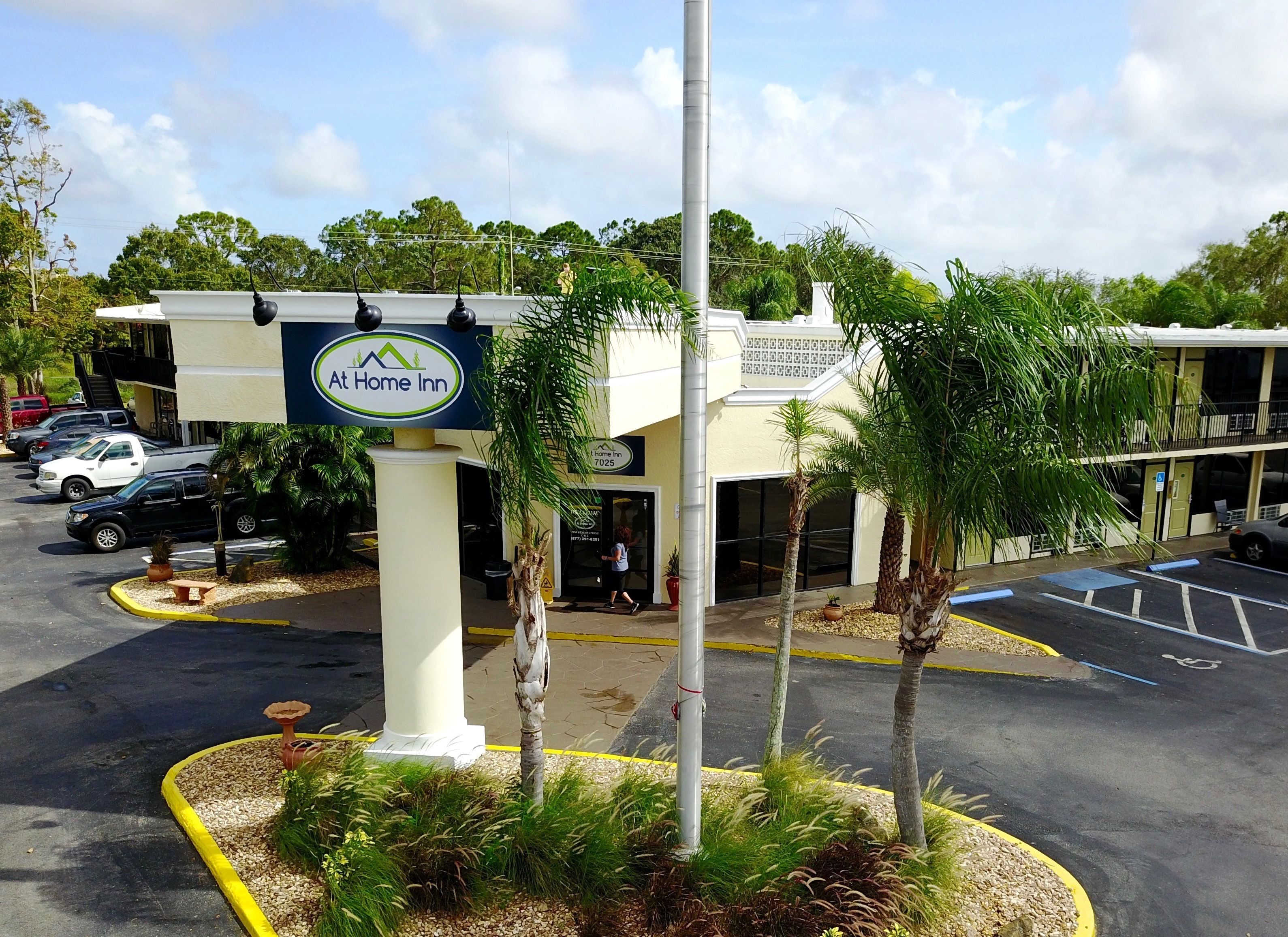 A hotel with a sign reading "At Home Inn," parking spaces, and a few palm trees.