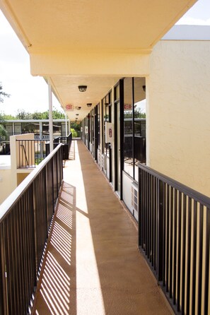 A covered corridor with a metal railing, a concrete floor, and a view of the outside.
