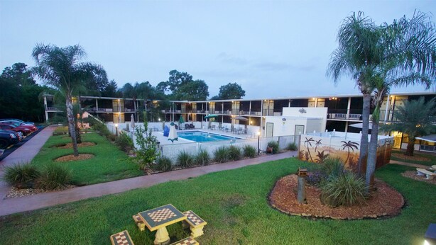 A hotel with a swimming pool, outdoor seating, and a well-maintained lawn.