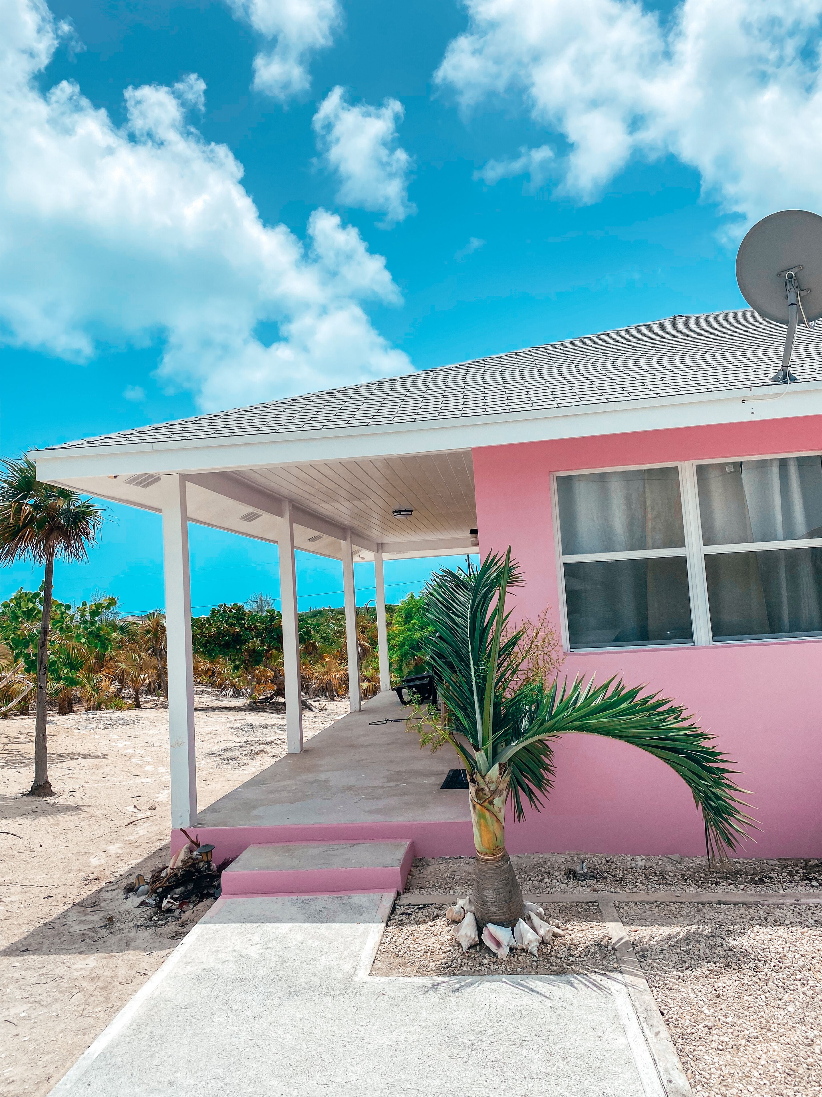 A pink building with a covered porch, a satellite dish, and a view of the beach.