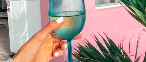 A hand holding a clear glass with a blue tint, palm tree, and a pink building with a white door in the background.