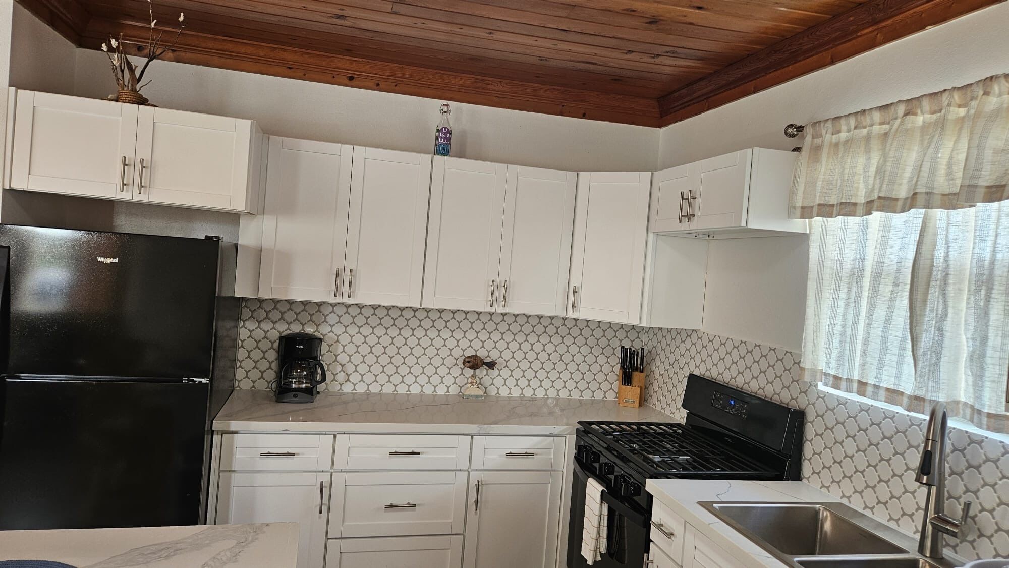 A kitchen with white cabinets, a black refrigerator, a coffee maker, and a stove.