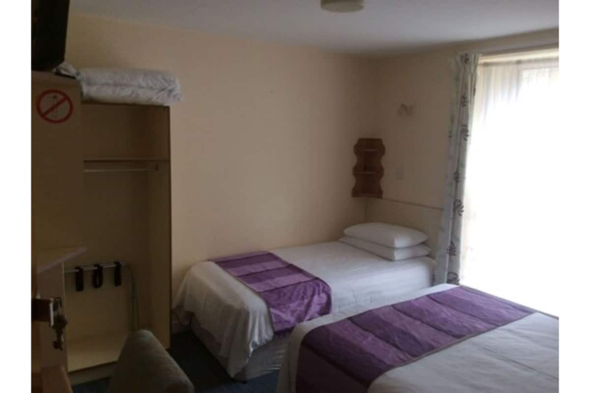 A hotel room with two beds, a wardrobe, and a wooden headboard.