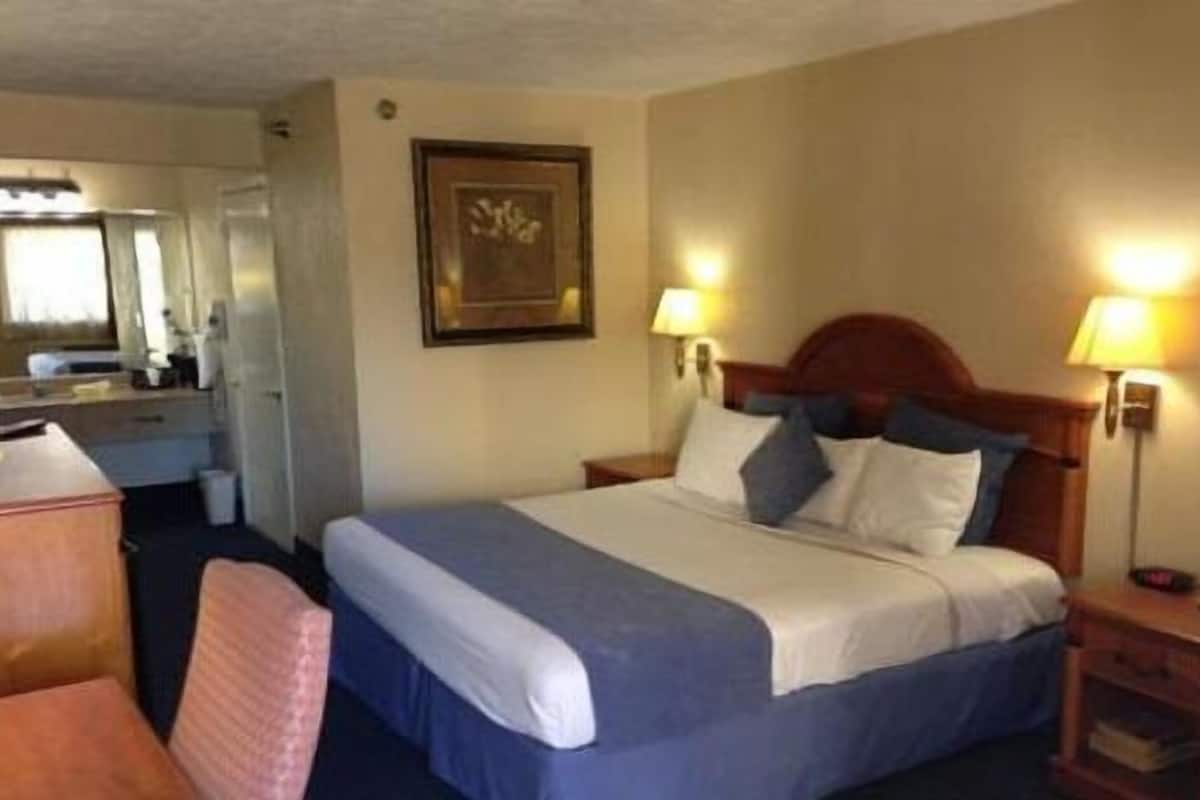 Ett hotellrum med en säng, sänglampor, ett skrivbord och en stol.