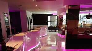 Un moderno vestíbulo de hotel con un mostrador de recepción curvo, un área de descanso con mesas y sillas, y un gran ventanal que proporciona luz natural.