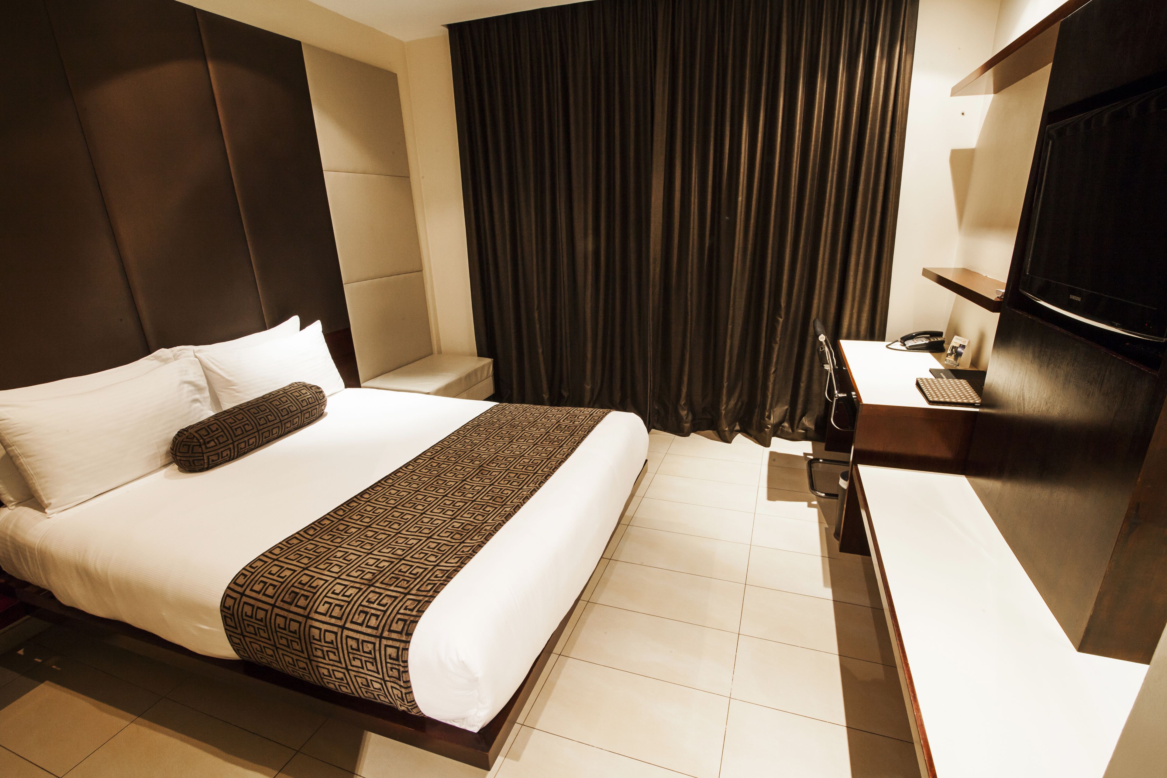 A hotel room with a large bed, a desk with a computer, a telephone, and a television.