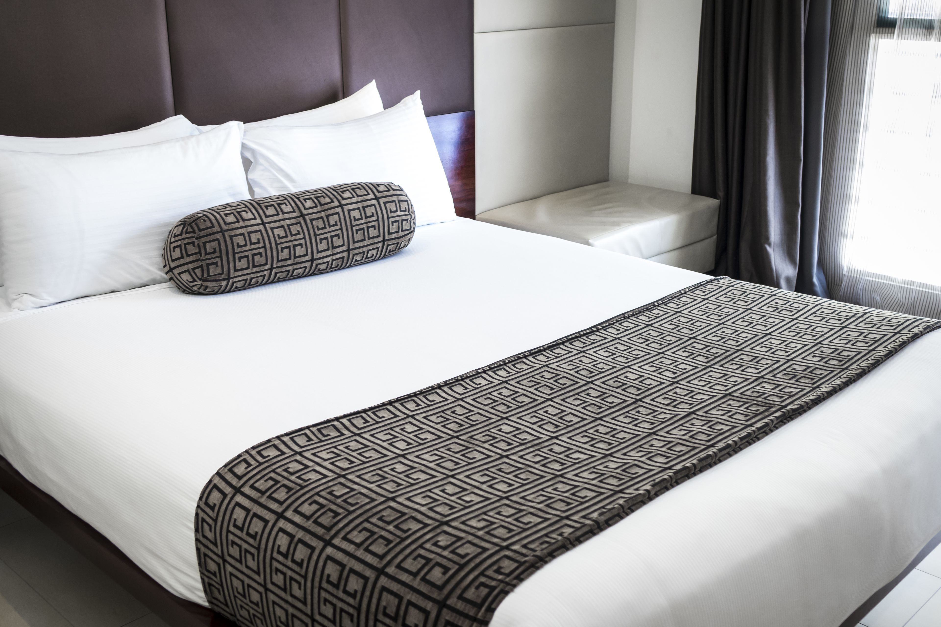 Una cama bien hecha con sábanas blancas, un edredón estampado y una almohada decorativa.