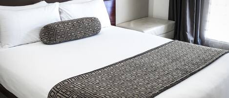 Una cama bien hecha con sábanas blancas, un edredón estampado y una almohada decorativa.
