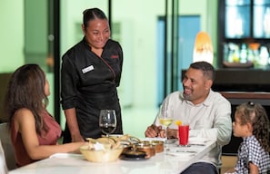Um restaurante com uma mesa posta para quatro pessoas, incluindo um garçom, um homem, uma mulher e uma criança.