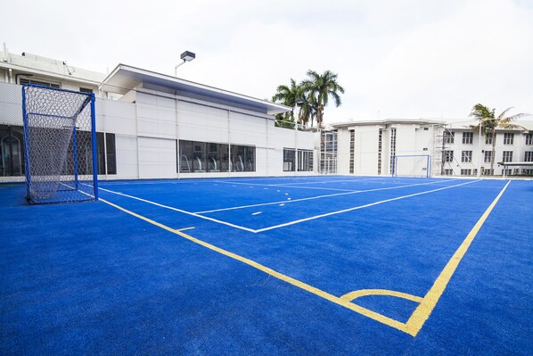An outdoor basketball court with a blue surface and yellow lines, surrounded by buildings and palm trees. - Lamana Hotel (Port Moresby)