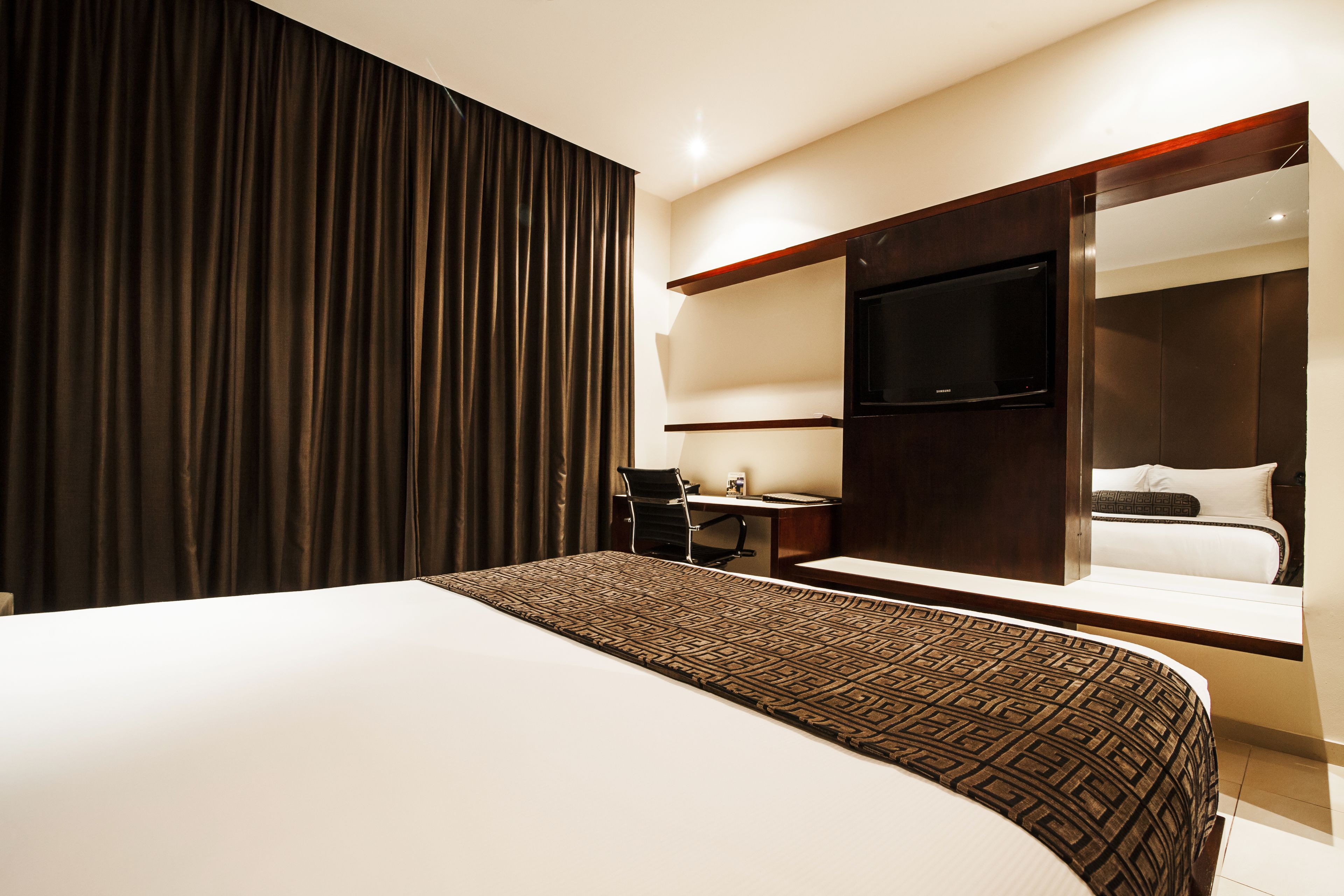 A hotel room with a large bed, a desk with a chair, a television, and a wardrobe.